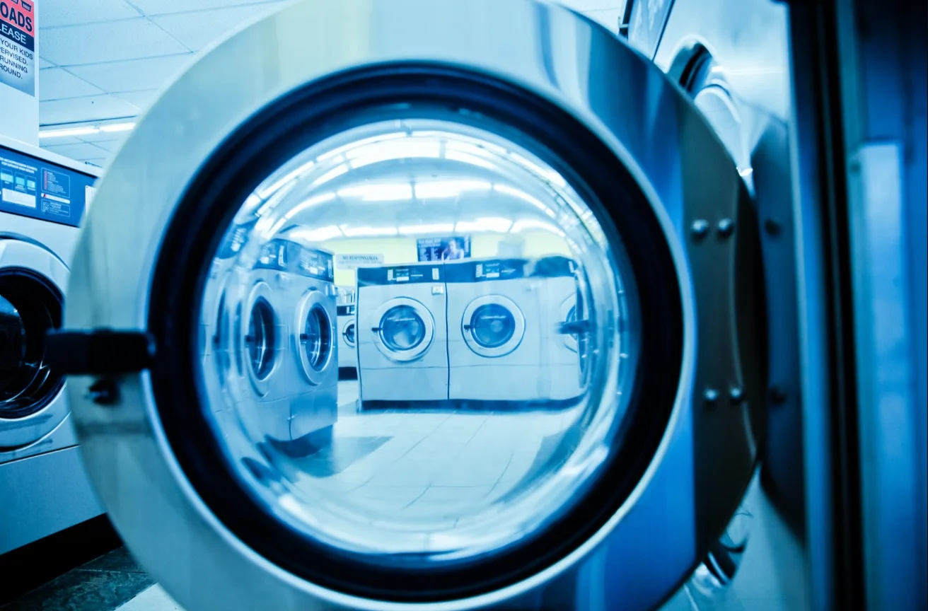 Front-loading laundry machines reflected in an open washer door